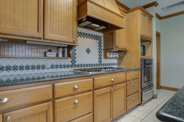 kitchen with premium range hood, appliances with stainless steel finishes, dark stone countertops, light tile patterned floors, and crown molding