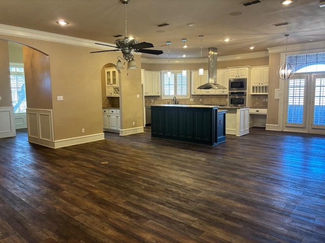 kitchen featuring decorative light fixtures, white cabinetry, island exhaust hood, stainless steel appliances, and a center island with sink