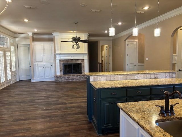 kitchen with decorative light fixtures, sink, light stone countertops, a center island, and a brick fireplace