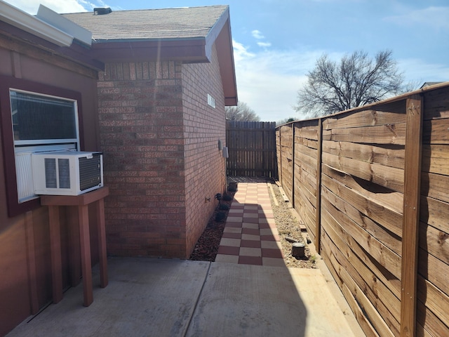 view of home's exterior with brick siding, a shingled roof, a patio area, cooling unit, and a fenced backyard