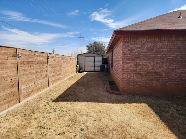 view of yard with central air condition unit, a storage shed, a fenced backyard, and an outdoor structure