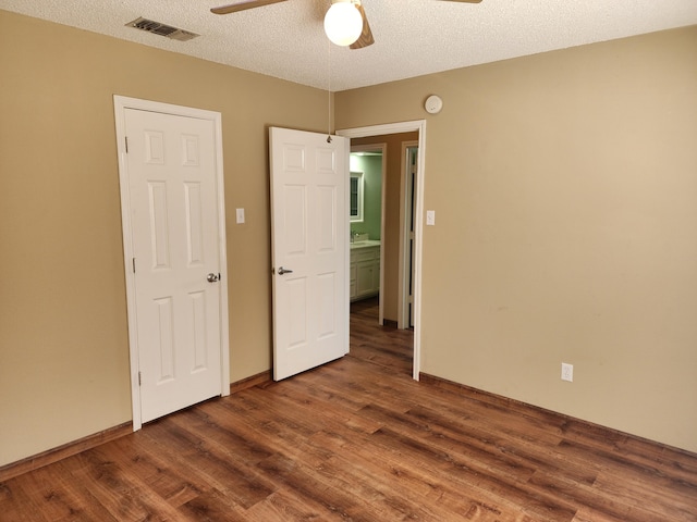 unfurnished bedroom featuring ceiling fan, visible vents, dark wood finished floors, and a textured ceiling