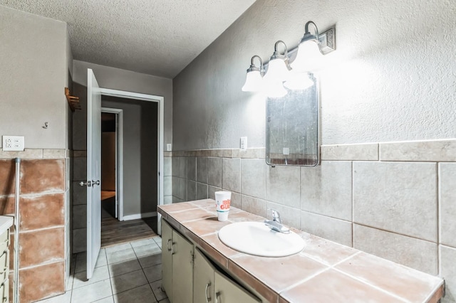 bathroom featuring vanity, tile patterned flooring, tile walls, and a textured ceiling