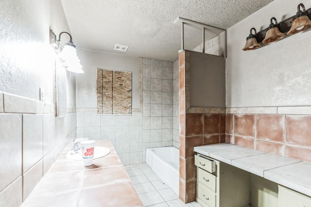 bathroom featuring tile walls, vanity, a textured ceiling, a tub to relax in, and tile patterned floors