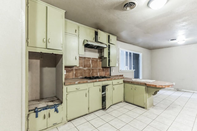 kitchen featuring tasteful backsplash, a textured ceiling, gas cooktop, kitchen peninsula, and green cabinets