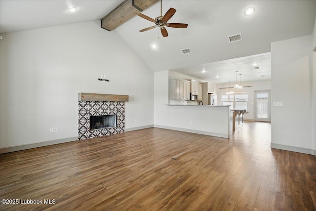 10330 Ave X Ave, Lubbock, TX 79423 - unfurnished living room featuring ceiling fan, beamed ceiling, wood finished floors, high vaulted ceiling, and a fireplace
