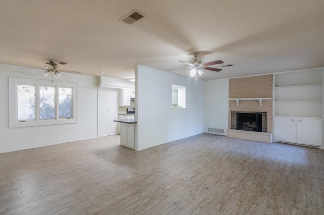 unfurnished living room with a brick fireplace, light wood-type flooring, ceiling fan, and plenty of natural light