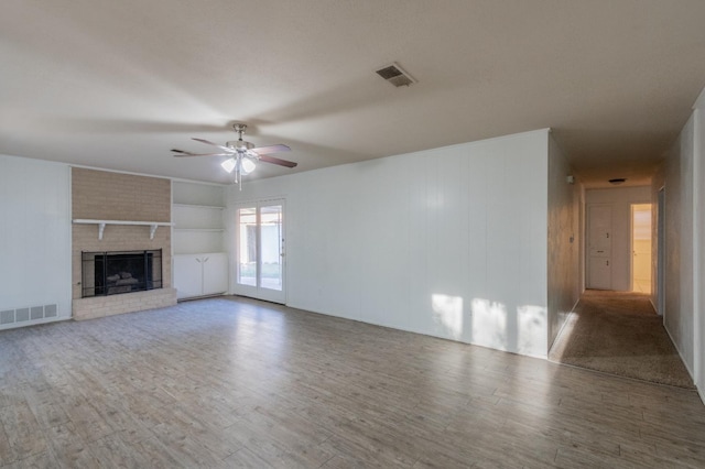 unfurnished living room featuring ceiling fan, built in features, wood-type flooring, and a brick fireplace