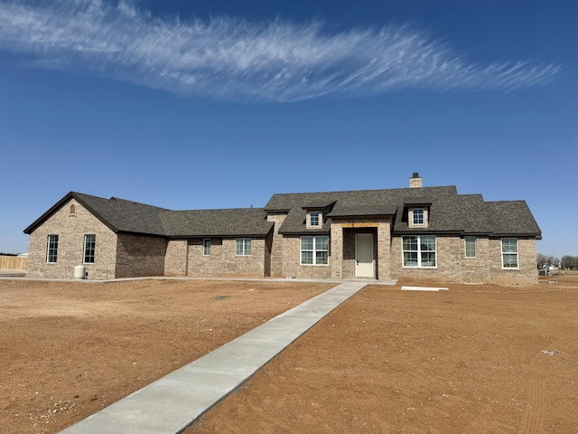 view of front facade featuring a shingled roof, a chimney, a front yard, and brick siding