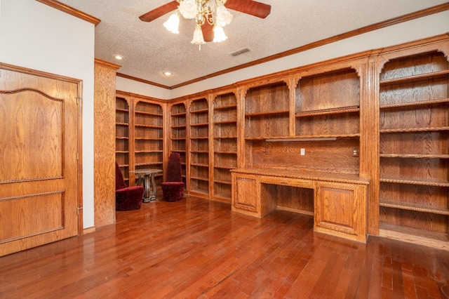 unfurnished office with dark wood-type flooring, crown molding, built in desk, a textured ceiling, and ceiling fan