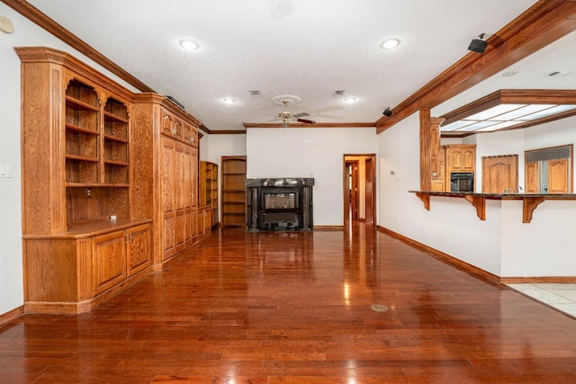 unfurnished living room featuring crown molding, ceiling fan, dark wood-type flooring, and a textured ceiling