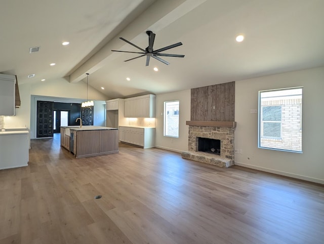 kitchen with lofted ceiling with beams, hanging light fixtures, a center island with sink, and light hardwood / wood-style flooring