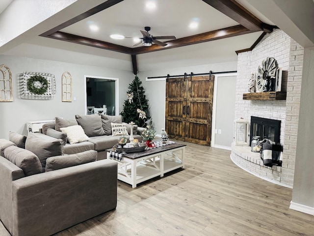 living room with a fireplace, a raised ceiling, ceiling fan, a barn door, and light hardwood / wood-style floors