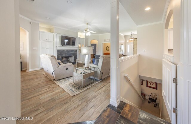 5004 County Rd 1430, Lubbock, TX 79407 - living room with arched walkways, ceiling fan, crown molding, a fireplace, and wood finished floors