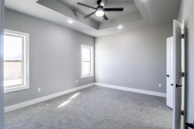 carpeted spare room featuring a tray ceiling and ceiling fan