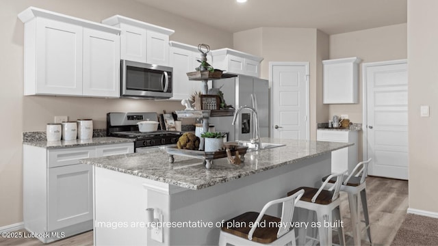 2337 149th St, Lubbock, TX 79423 - kitchen with appliances with stainless steel finishes, white cabinetry, a kitchen island with sink, a breakfast bar, and light stone counters