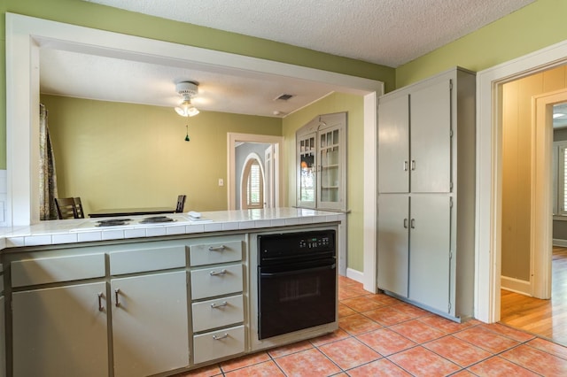 kitchen with white cooktop, a textured ceiling, light tile patterned flooring, tile countertops, and oven