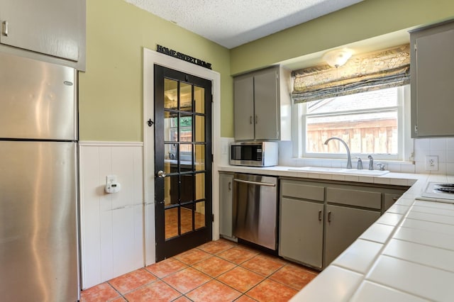 kitchen with sink, gray cabinetry, a textured ceiling, appliances with stainless steel finishes, and tile counters