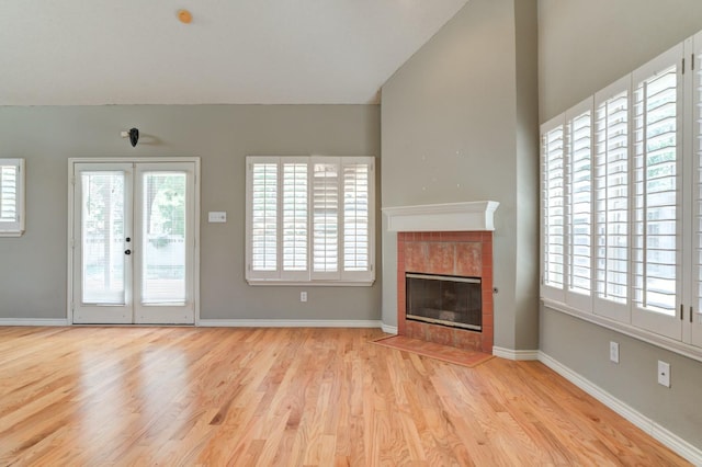 unfurnished living room with lofted ceiling, a fireplace, light hardwood / wood-style floors, and a healthy amount of sunlight