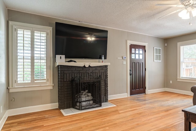 living room featuring ceiling fan, a brick fireplace, a textured ceiling, and light hardwood / wood-style flooring