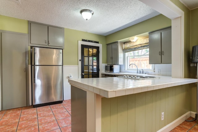 kitchen featuring tile counters, stainless steel fridge, light tile patterned floors, and kitchen peninsula