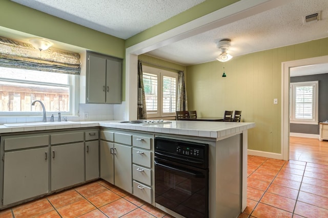 kitchen featuring tile countertops, sink, light tile patterned floors, kitchen peninsula, and white gas cooktop