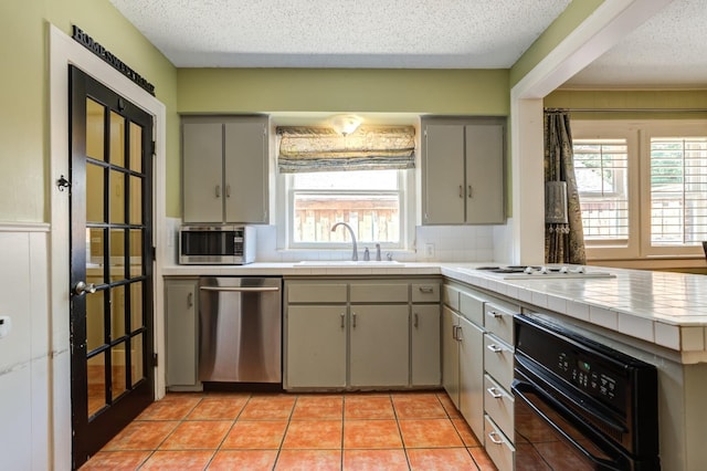 kitchen featuring light tile patterned flooring, sink, a textured ceiling, appliances with stainless steel finishes, and tile counters