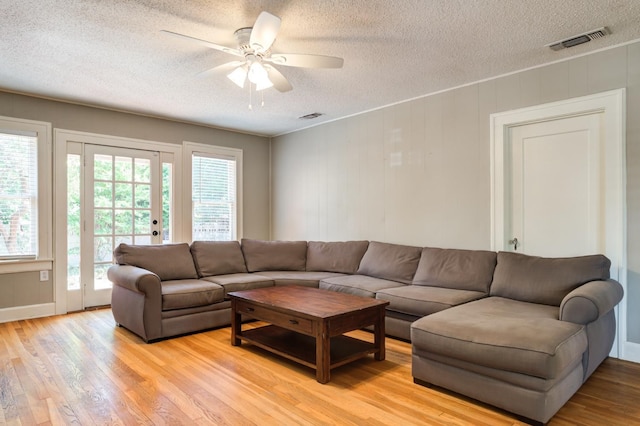 living room featuring ceiling fan, light hardwood / wood-style floors, and a textured ceiling