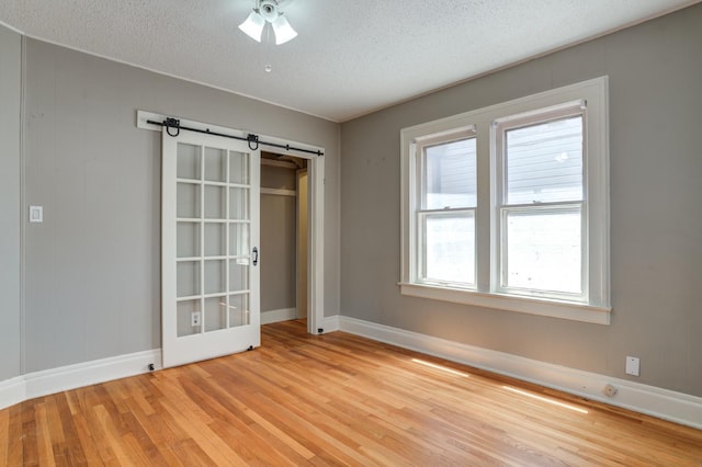 empty room featuring a barn door, a textured ceiling, and light wood-type flooring