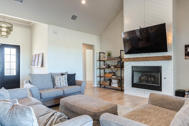 living room featuring a notable chandelier, light hardwood / wood-style floors, a large fireplace, and high vaulted ceiling