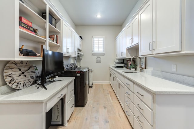 kitchen featuring sink, light stone counters, light wood-type flooring, washing machine and dryer, and white cabinets