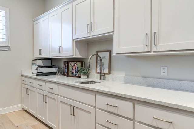 kitchen with white cabinetry, sink, light stone counters, and light hardwood / wood-style flooring