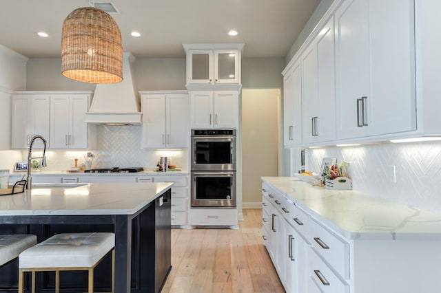 kitchen featuring double oven, hanging light fixtures, light stone counters, tasteful backsplash, and white cabinets