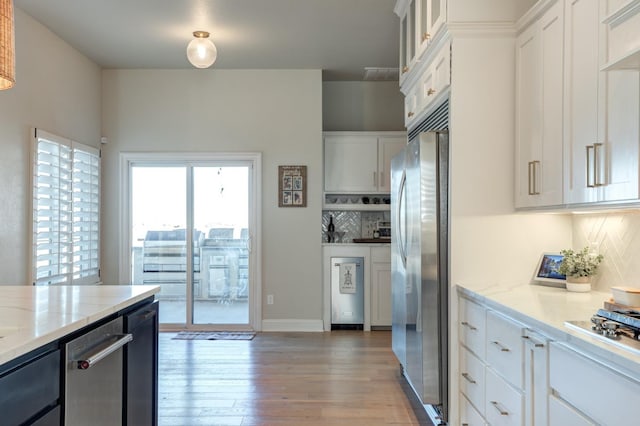 kitchen with white cabinetry, tasteful backsplash, light hardwood / wood-style flooring, stainless steel fridge, and light stone countertops