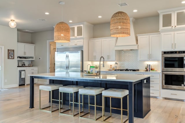 kitchen with hanging light fixtures, an island with sink, white cabinets, and appliances with stainless steel finishes