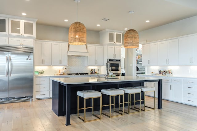 kitchen with white cabinetry, backsplash, hanging light fixtures, a kitchen island with sink, and stainless steel appliances