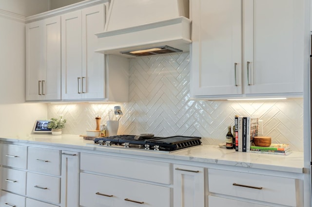 kitchen featuring tasteful backsplash, white cabinetry, stainless steel gas cooktop, light stone counters, and custom range hood