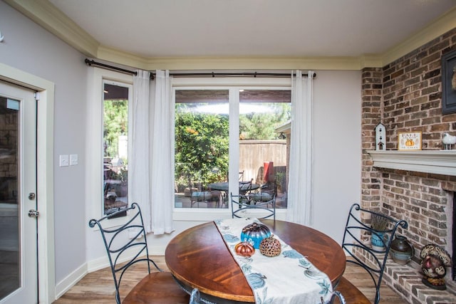 dining area featuring wood-type flooring, plenty of natural light, crown molding, and a brick fireplace