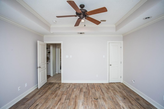 empty room with crown molding, wood-type flooring, and a raised ceiling