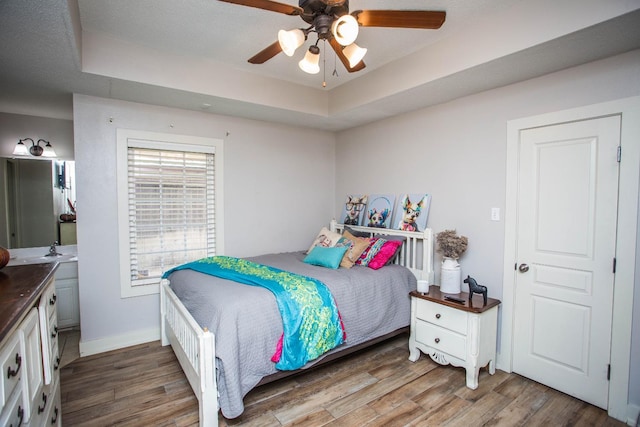 bedroom featuring ceiling fan, hardwood / wood-style floors, connected bathroom, a textured ceiling, and a raised ceiling