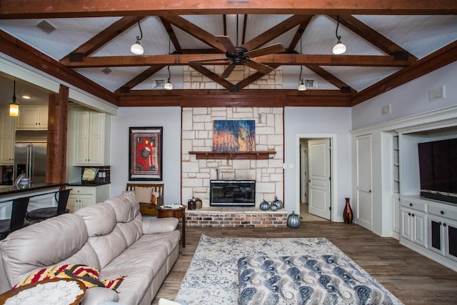 living room with hardwood / wood-style flooring, ceiling fan, a stone fireplace, and lofted ceiling with beams