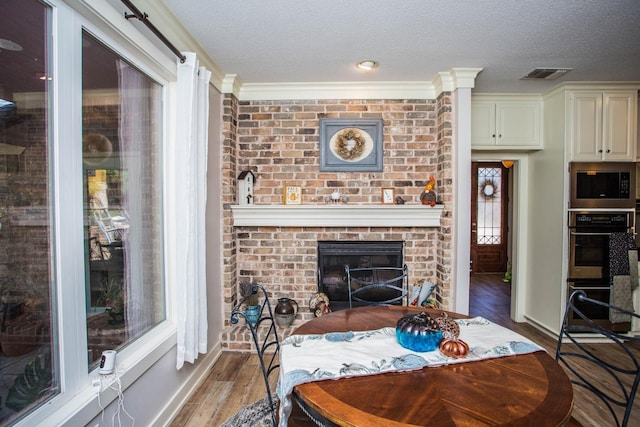 dining room with wood-type flooring, a brick fireplace, and a textured ceiling