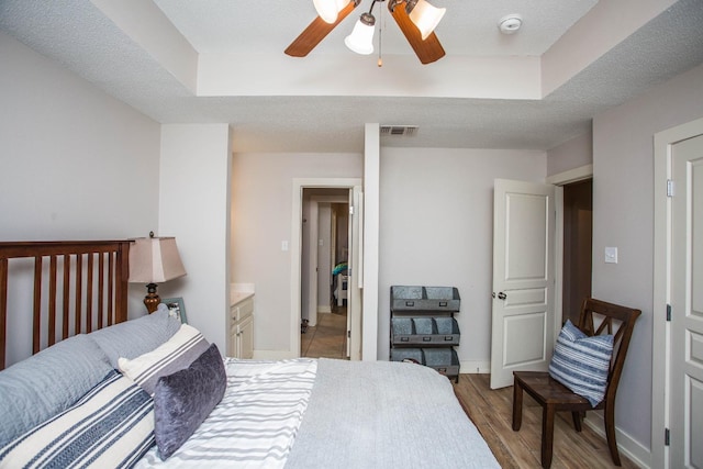 bedroom with ceiling fan, light hardwood / wood-style floors, a raised ceiling, and a textured ceiling