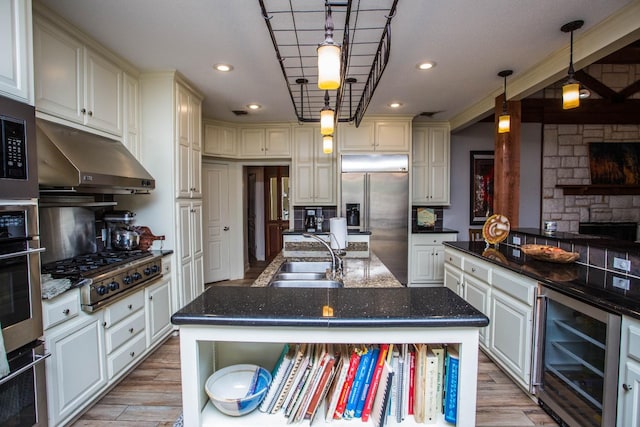 kitchen with sink, wine cooler, hanging light fixtures, stainless steel appliances, and a center island with sink