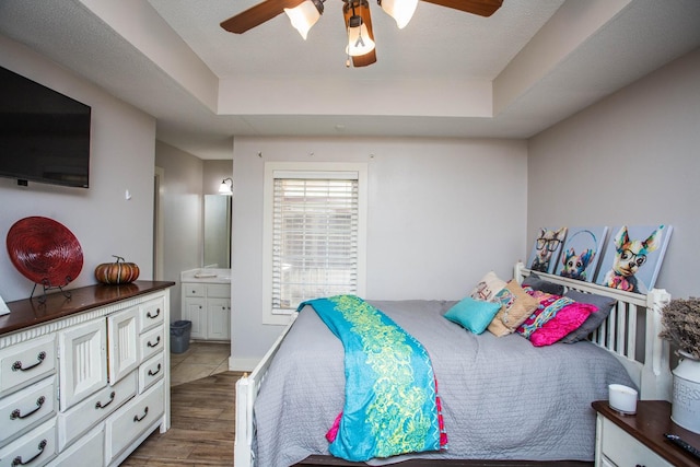 bedroom with dark wood-type flooring, connected bathroom, ceiling fan, and a tray ceiling