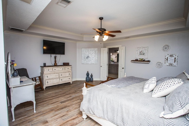 bedroom featuring crown molding, a tray ceiling, wood-type flooring, and ensuite bathroom