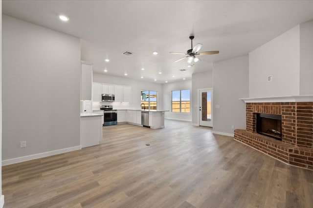 unfurnished living room featuring light hardwood / wood-style flooring, sink, a fireplace, and ceiling fan