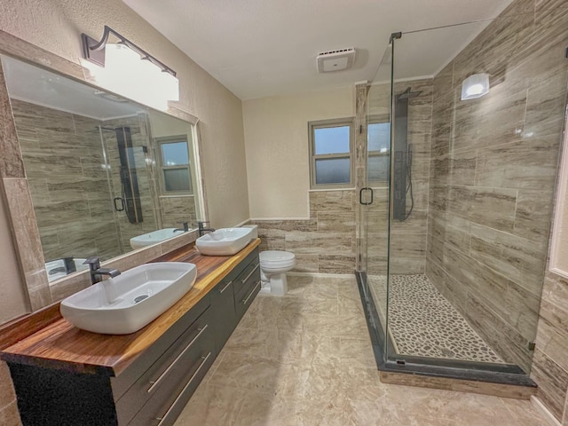 bathroom featuring vanity, toilet, a shower with door, and tile walls