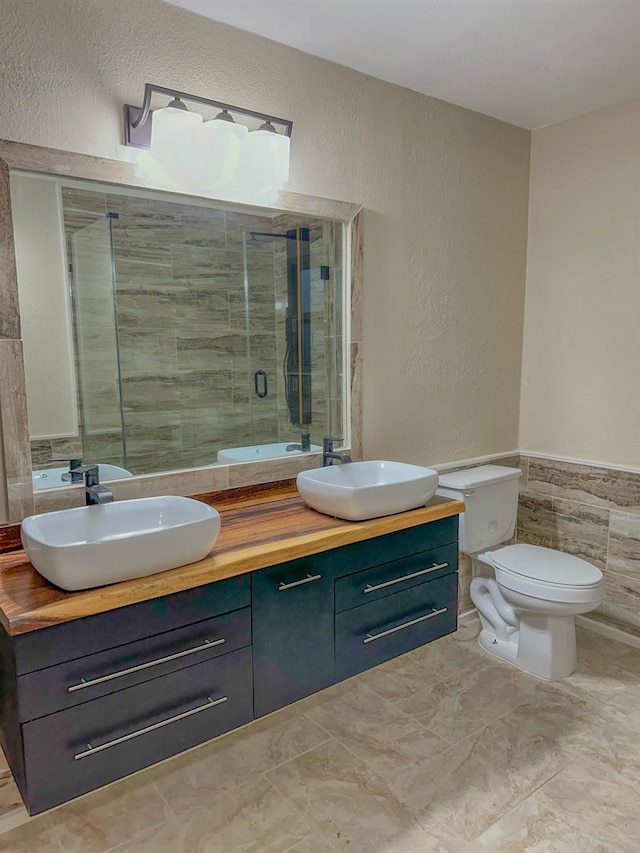 bathroom with vanity, toilet, a shower with door, and tile walls