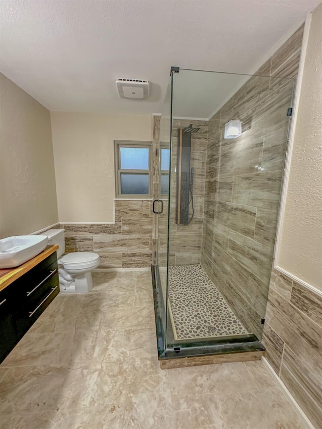 bathroom featuring a shower with door, vanity, tile walls, and toilet